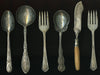 A row of antique silverware (three spoons, two forks and one knife) on a black background