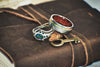 A brown leather-bound book with two silver rings and a gold key on top. One of the rings has a large green stone.